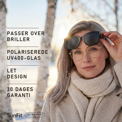 Kvinde med briller løfter SunFit fit-over-solbriller i vintersol over sne